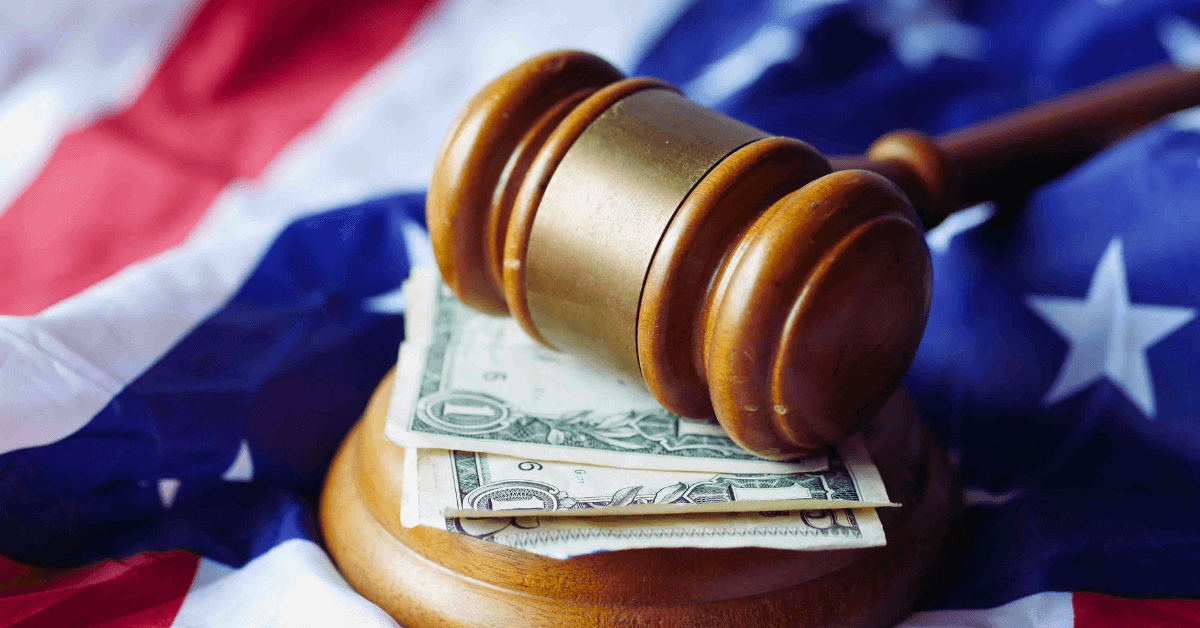 Gavel resting on top of folded pile of $1 bills and an American flag